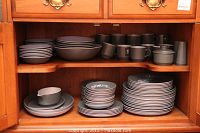 Photo showing full dinnerware set including plates, bowls, cups, sugar bowl, and creamer inside a pine cabinet