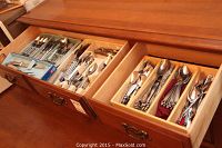 Two open drawers of wooden flatware organizer holding assorted stainless steel cutlery
