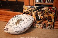 Photo of white football with Hamilton Tiger-Cats logo and multiple signatures in black marker, alongside a football history book with a collage cover.