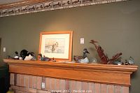 Wide view of mantel displaying various duck decoys, framed duck print, and wood bird sculpture