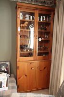 Full view of pine cabinet with glass doors showing shelves containing items, lower closed wood cabinets.