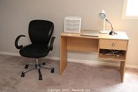 Overall view of the desk, office chair, and desk lamp in a room with beige carpet and walls.