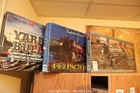 Three boxed Presidents Choice train sets displayed on top of a cabinet. Includes Yard Builder Switcher Locomotive, 4-6-2 Pacific, and Big 10 Express models.