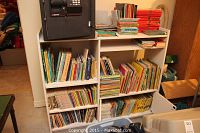 Photo showing white cubic shelving unit filled with various books including colorful children's books and comics.