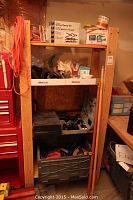 Photo of wood shelving unit loaded with tools, hardware boxes, jars and plastic crates containing various hand and power tools.