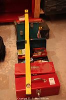 Photo showing two red metal tool boxes, a green tool box, and a yellow spirit level placed across the tool boxes on the floor