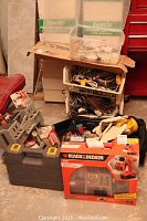 Wide shot showing cordless drill kit box, Ryobi Jobmate drill case, plastic boxes with small parts, baskets of cords, and various tools stacked.