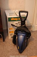 Simoniz blue power washer unit with black handle and coiled hose in front of Shop-Vac box