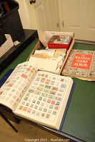 Open blue hardcover album with mounted stamps, partially visible Majestic Stamp Album cover and box of loose stamps