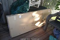 Photo of boxed arbor with gate still sealed, placed on a porch floor.