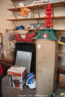 Photo shows a boxed Rigid wet dry vacuum, Christmas tree stand on top of a cardboard box, red plaid dog bed, white basket with dog items, and miscellaneous household items on shelves.