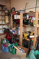 Full view of wooden shelving unit with assorted car-related tools, accessories, and paint cans. Includes green and orange hand tool, plastic crates, and various parts.