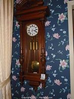 Full front view showing carved wooden case, decorative crest, columns, pendulum and weights