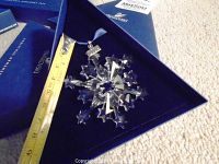 Photo of the clear crystal snowflake hanging ornament inside original blue Swarovski box beside measuring tape showing size approximately 8 cm.
