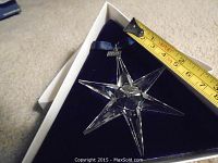 Clear Swarovski crystal snowflake ornament on blue felt cushion inside white box alongside measuring tape.