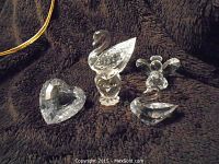 Photo showing four Swarovski crystal figurines on a dark textured surface: swan, angel, heart-shaped ornament, and owl figurine