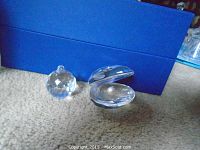 Clear faceted Swarovski crystal clam with white pearl inside next to faceted crystal ball on carpet with blue box background