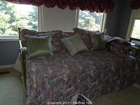 Front view of brass day bed with bedding and decorative pillows in muted tones.