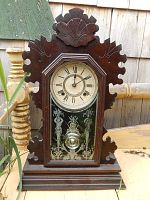 Front view of walnut case gingerbread clock showing octagonal bezel, Roman numeral dial, and etched glass door with visible brass pendulum.
