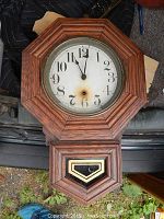 Front view of Sessions octagonal oak wall clock with glass pendulum window, showing clock face with staining and black Arabic numerals.