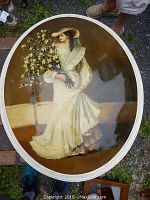 Full frontal view of the hand painted convex oval wall art featuring a woman in white dress with bouquet of flowers.