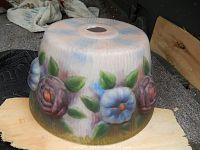 Image showing bottom side of a round older glass lamp shade with painted flowers including purple and blue blooms and green leaves on ribbed glass.