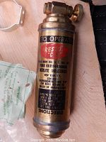 Close up of brass mini fire extinguisher showing label and operating instructions.