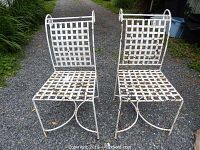Pair of white painted metal garden chairs, showing their full front view on gravel surface.