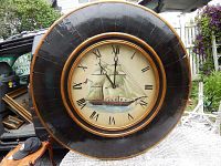 Full front view of large round black and blood orange wall clock with a sailing ship image on the face.