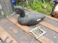 Wood duck decoy painted black with white spots and orange eyes, placed on wooden table with background objects and person partly visible