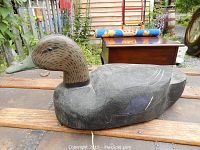 Side view of the early wood carved and hand painted duck decoy showing detailed feather paintwork and green bill, placed on wooden surface outdoors.