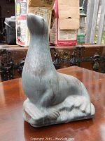 Front and side view of matte blue Blue Mountain Pottery seal figurine on a wooden table with black metal trunks in the background.