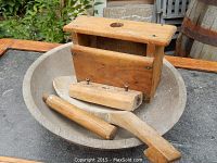 Wooden treen bowl containing a wooden paddle and wooden press placed on an outdoor surface.