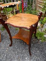 Maple wood side table with curved legs and shaped top surface, photo taken outdoors with surrounding garden background.