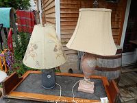 Full view of both lamps on wooden tray showing the dark base lamp with floral fabric shade and taller pink ceramic lamp with cream shade.