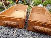 Two old oak wood desk drawers side-by-side on gravel, showing carved handles and interior wear.