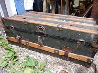 Full view of antique steamer trunk showing green canvas or leather body with wood slats and metal latches and hardware.