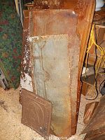 Stack of large rusted tin side molding panels against wall with one smaller decorative embossed panel in front.