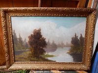 Frontal image of the framed Victorian era oil painting depicting a river landscape with trees and clouds.