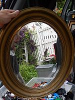 Front view of the older oval wood framed mirror with worn gold-toned frame and clear glass.