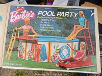 Front of original Mattel Barbie's Pool Party box showing 16" x 5" pool with floral decorative graphics, ladder/slide, diving board, and floating chaise lounge. Dolls not included.