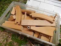 Clear plastic tote container filled with various maple wood toy blocks and pieces including large rectangular blocks and curved track pieces.