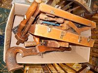 Photo showing various older wooden woodworking tools and clamps packed in a cardboard box.