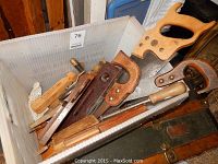 Photo of a collection of antique and vintage hand tools in a plastic container. Visible are wooden hand saws, wooden hand planes, a hand brace, rasp files, and other woodworking tools.