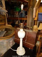 Full view of the white Aladdin Alacite table lamp with original finial on top, placed on wooden surface surrounded by vintage items.