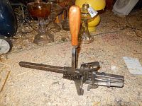 Full view of Waller woodworking tool with a wooden handle standing on a workshop surface among old lamps and tools.