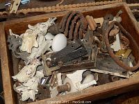 Box containing various antique door hardware including ceramic knobs, metal hinges, decorative plates, and rusty handles.