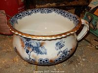 Front left angle of antique thunder mug showing floral pattern and gold rim with handle on right side