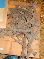 Cast iron fencing parts piled on wooden surface with identifiable leaf designs and curved metal sections for ornamental fencing.