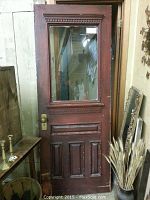 Full view of the old wooden door with window, showing the red-brown wood with wear and the brass door handle.